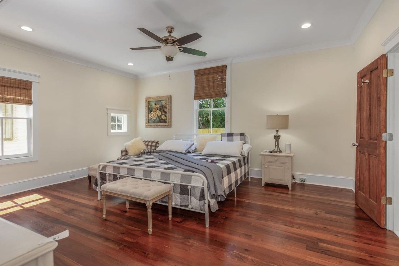 A bedroom with a bed, a nightstand, a window with blinds, a ceiling fan, and hardwood flooring.