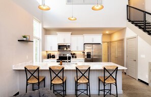 A modern kitchen with a central island, bar stools, stainless steel appliances, and pendant lighting. - ✨ Modern 2BR Lyndon Loft Oasis | Work & Play| Private Patio | 2-Car Garage (Louisville)