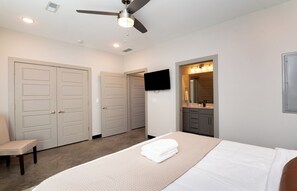 A bedroom with a bed, a ceiling fan, a TV mounted on the wall, and a bathroom with a mirror and sink. - ✨ Modern 2BR Lyndon Loft Oasis | Work & Play| Private Patio | 2-Car Garage (Louisville)