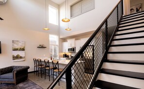 A modern kitchen with white cabinets, a dining area with a marble countertop, and a staircase with black railings. - ✨ Modern 2BR Lyndon Loft Oasis | Work & Play| Private Patio | 2-Car Garage (Louisville)