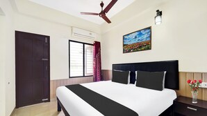 A bedroom with a bed, a ceiling fan, a window with curtains, a nightstand, a vase with flowers, and a painting on the wall. - Hotel O Technopark Formerly Le Frank (Trivandrum)