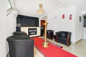 A hotel reception area with a reception desk, black leather sofas, a red carpet, and a chandelier.