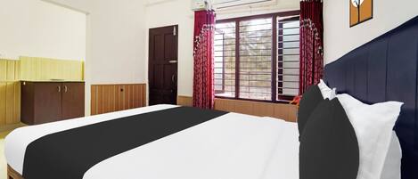 A hotel room with a bed, a wardrobe, a window with curtains, an air conditioning unit, and a wall clock.