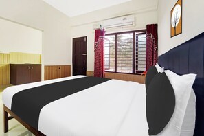 A hotel room with a bed, a wardrobe, a window with curtains, an air conditioning unit, and a wall clock.