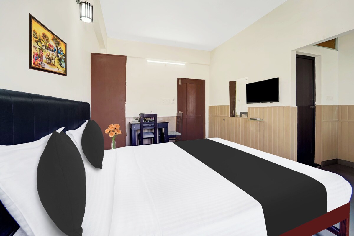 A hotel room with a bed, a desk, a chair, a TV, and a painting on the wall.