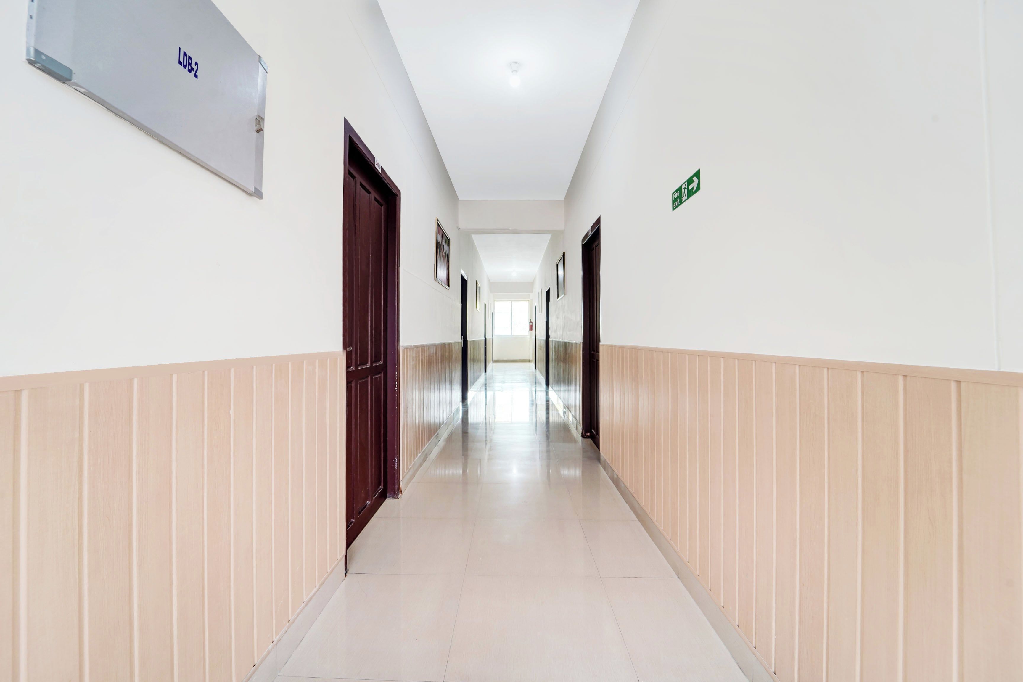 Un long couloir étroit, avec des portes de chaque côté, un panneau indiquant une sortie et un détecteur d’incendie sur le mur.