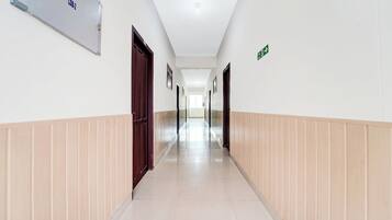 Un long couloir étroit, avec des portes de chaque côté, un panneau indiquant une sortie et un détecteur d’incendie sur le mur.