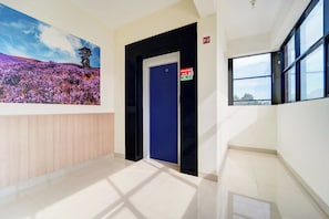 A hallway with a blue door, a fire exit sign, and a large window.