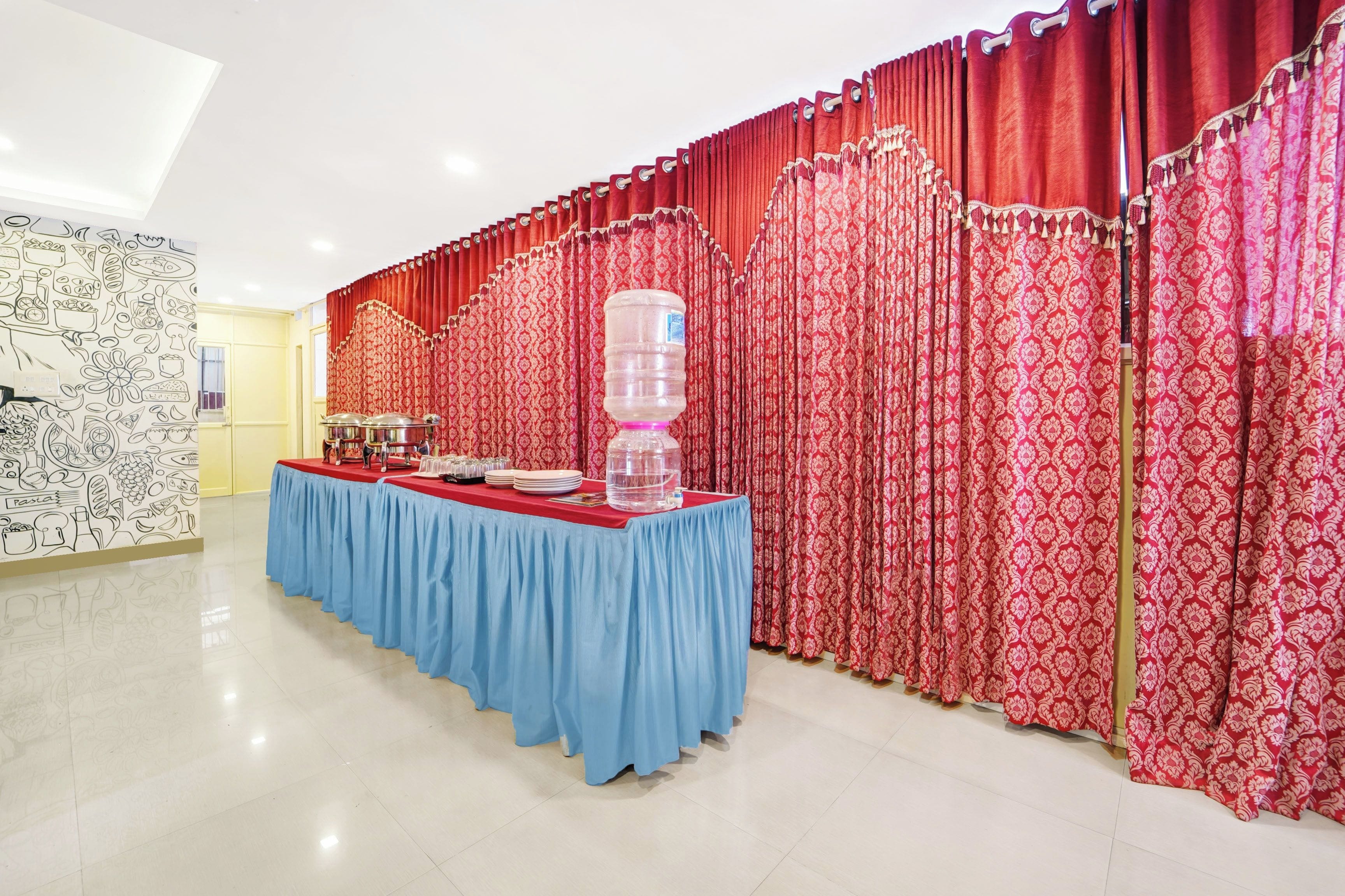 Un salón de banquetes con una larga mesa cubierta con mantel azul, cortinas rojas y un dispensador de agua.