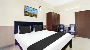 A hotel room with a bed, a desk, a chair, a wardrobe, and a painting on the wall. - Hotel O Technopark Formerly Le Frank (Trivandrum)