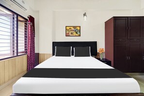 A hotel room with a bed, a nightstand, a wardrobe, a window with curtains, and a wall-mounted light fixture.