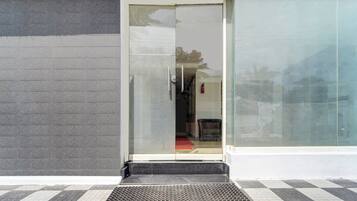 A building entrance with a glass door, a fire extinguisher, and a metal step leading up to the door.