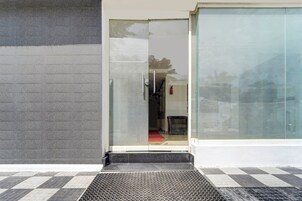 Entrada de un edificio con puerta de vidrio, extintor y un escalón metálico que lleva a la puerta.