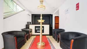 A hotel reception area with a red carpet, black leather chairs, a chandelier, and a reception desk. - Hotel O Technopark Formerly Le Frank (Trivandrum)
