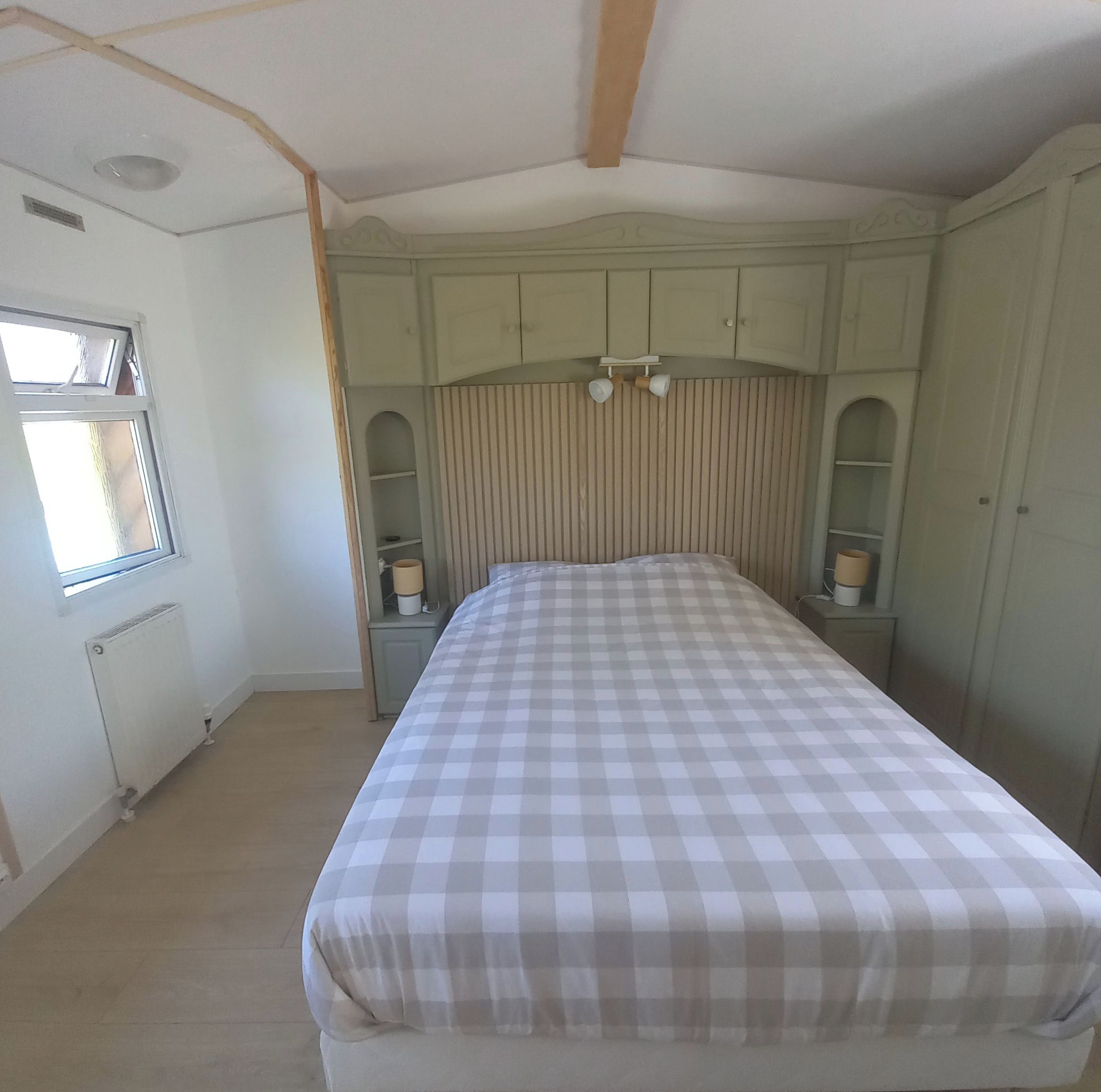 Een slaapkamer met een bed, een raam en inbouwkasten.