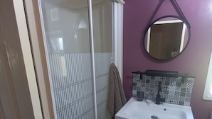 A bathroom with a glass shower enclosure, a white sink with a black faucet, and a mirror on the wall. - A Little Paradise (Sanghen)