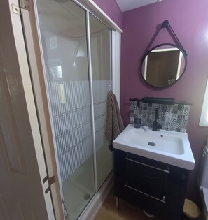 A bathroom with a glass shower enclosure, a white sink with a black faucet, and a mirror on the wall. - A Little Paradise (Sanghen)