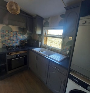 A compact kitchen with a gas stove, a built-in oven, a sink, and a window.