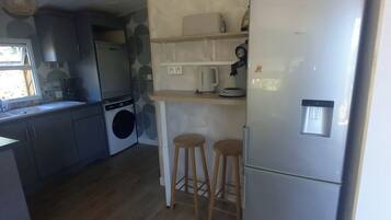 Een kleine keuken met een ingebouwde wasmachine, een koelkast, houten krukken en een hangende lamp.