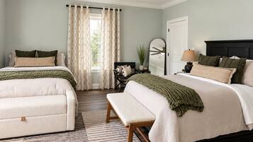 A bedroom with two beds, a ceiling fan, a window with curtains, a bedside table with a lamp, and a mirror.