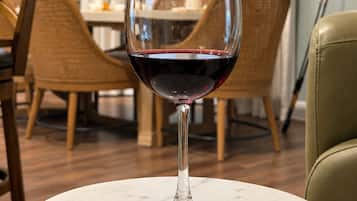 A wine glass on a marble table in a dining area with wicker chairs and a clock on the wall.