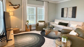 A modern living room with a sofa, armchairs, a coffee table, and a TV.