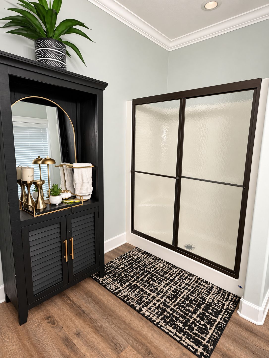 A bathroom with a black vanity, a large mirror, a potted plant, and a glass shower enclosure.