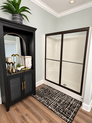 Une salle de bain avec un meuble-lavabo noir, un grand miroir, une plante en pot et une cabine de douche en verre.