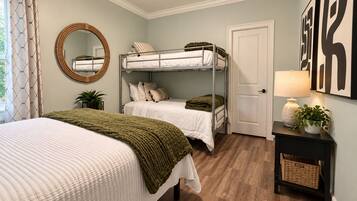 A bedroom with bunk beds, a round mirror, a bedside table with a lamp, and a door.
