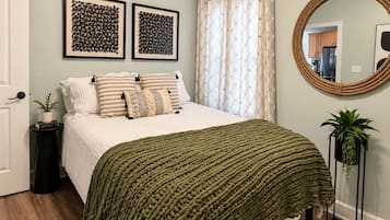 A bedroom with a bed, a ceiling fan, a round mirror, and two framed artworks on the wall.