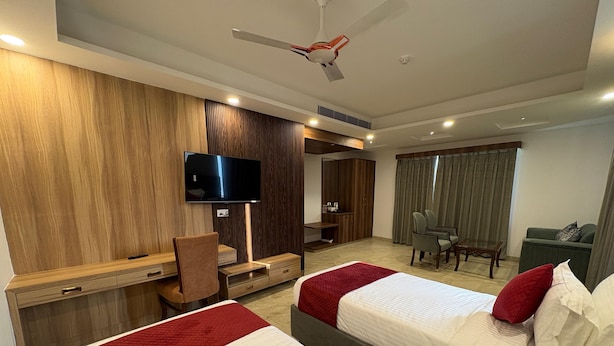 A hotel room with two beds, a desk, a TV, and a ceiling fan. - Hotel Jyoti International (Bodh Gaya)