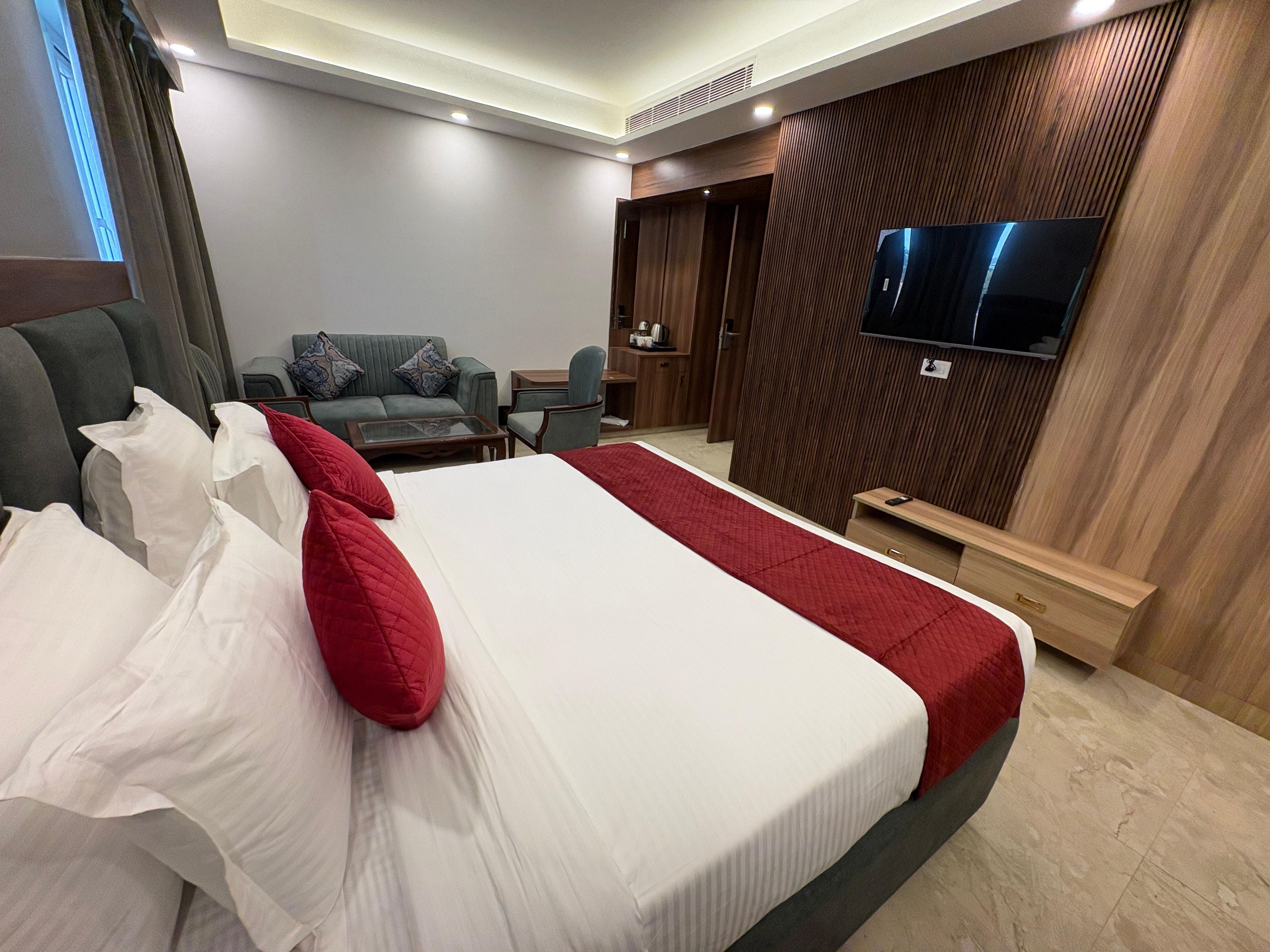 Habitación de hotel con una cama grande, televisor montado en la pared, zona de estar con sofá y sillones, y pared revestida de madera.