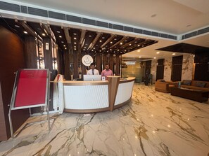 A hotel reception area with a marble floor, a reception desk, and a sign indicating a restaurant.