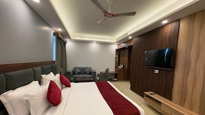 A modern hotel room with a large bed, a seating area with a sofa and armchairs, a television mounted on the wall, and a ceiling fan. - Hotel Jyoti International (Bodh Gaya)
