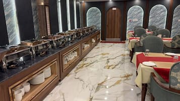 A hotel dining area with marble flooring, a buffet counter, and seating arrangements.