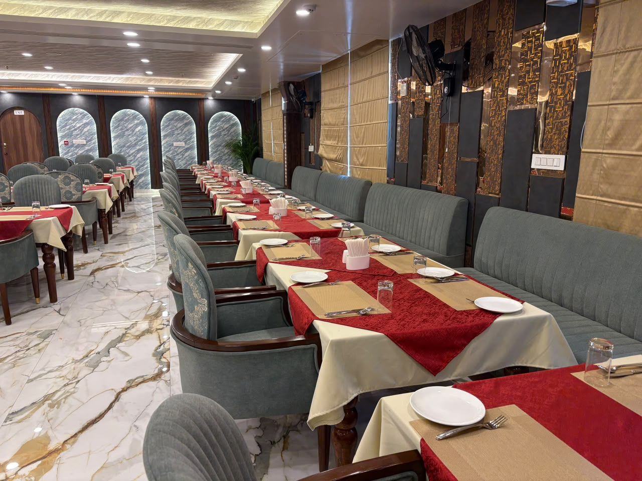 Un restaurante con mesas largas, manteles rojos y asientos tapizados en gris.