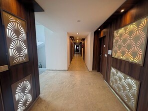 A hotel corridor with a long, straight path, wooden paneling on the walls, and a light-colored floor.