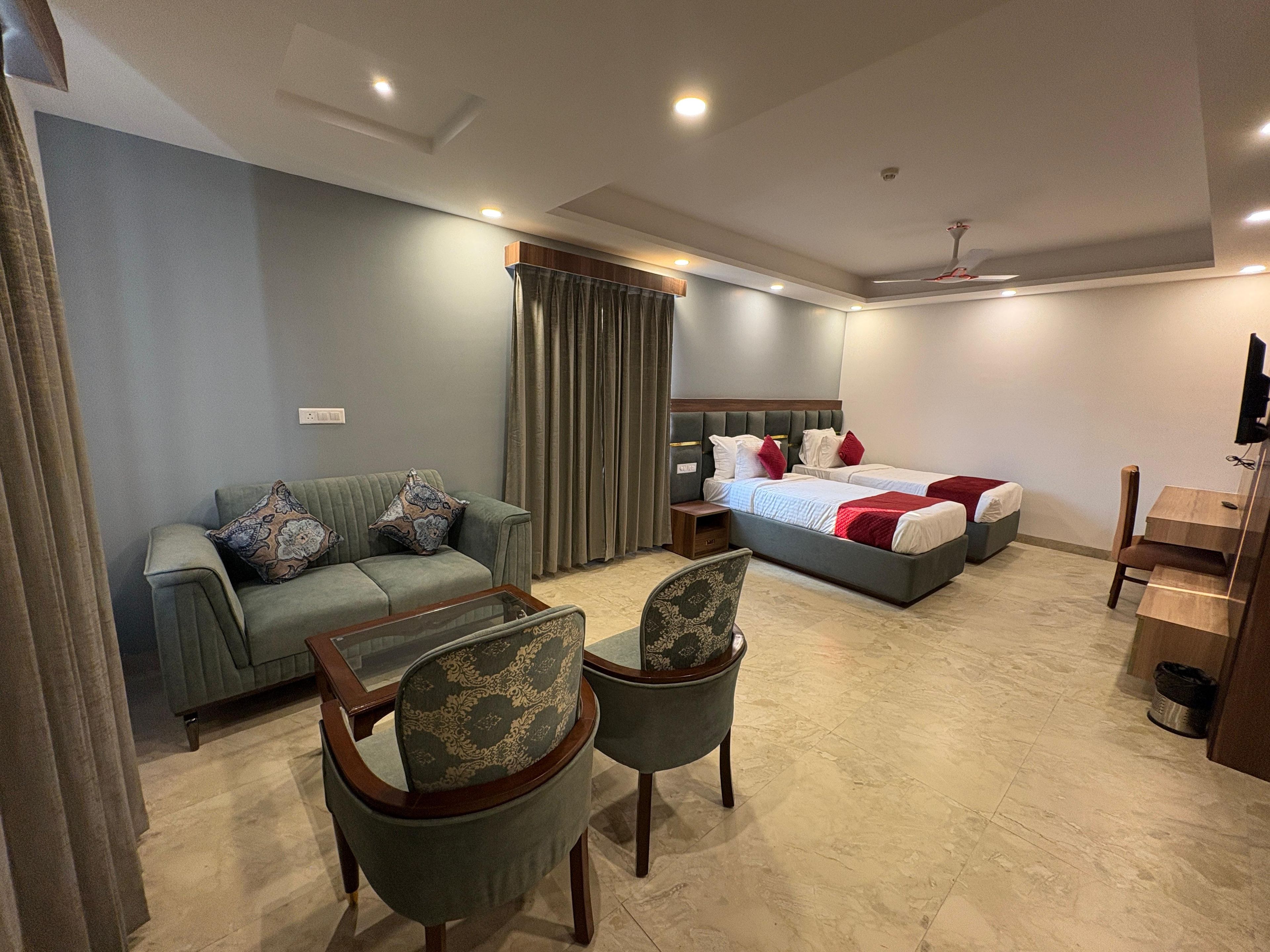 Habitació d'hotel amb sofà, dues cadires, un llit amb almoadins, televisió i escriptori.