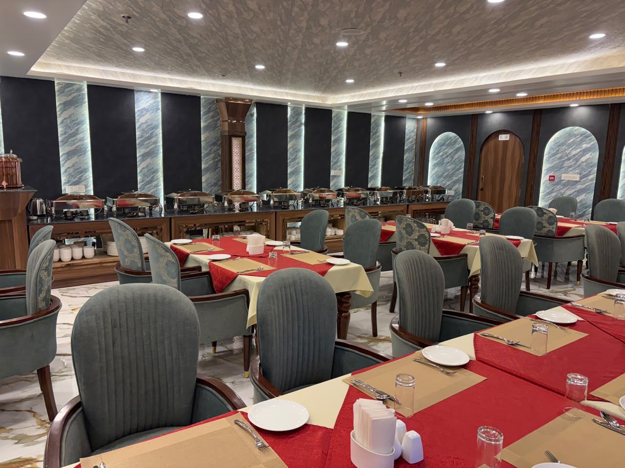 A hotel dining area with multiple tables set for guests, featuring a modern design with marble accents and a neutral color palette.
