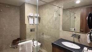 A modern bathroom with a glass-enclosed shower, a sink with a marble countertop, and a large mirror. - Hotel Jyoti International (Bodh Gaya)