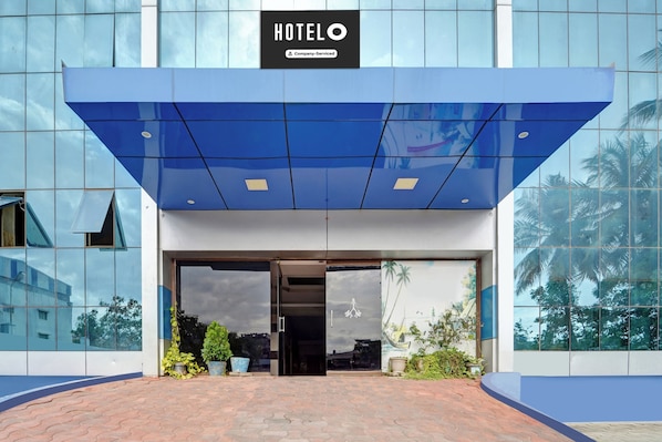 A hotel entrance with a blue awning, glass facade, and a sign indicating it's a company-serviced hotel.