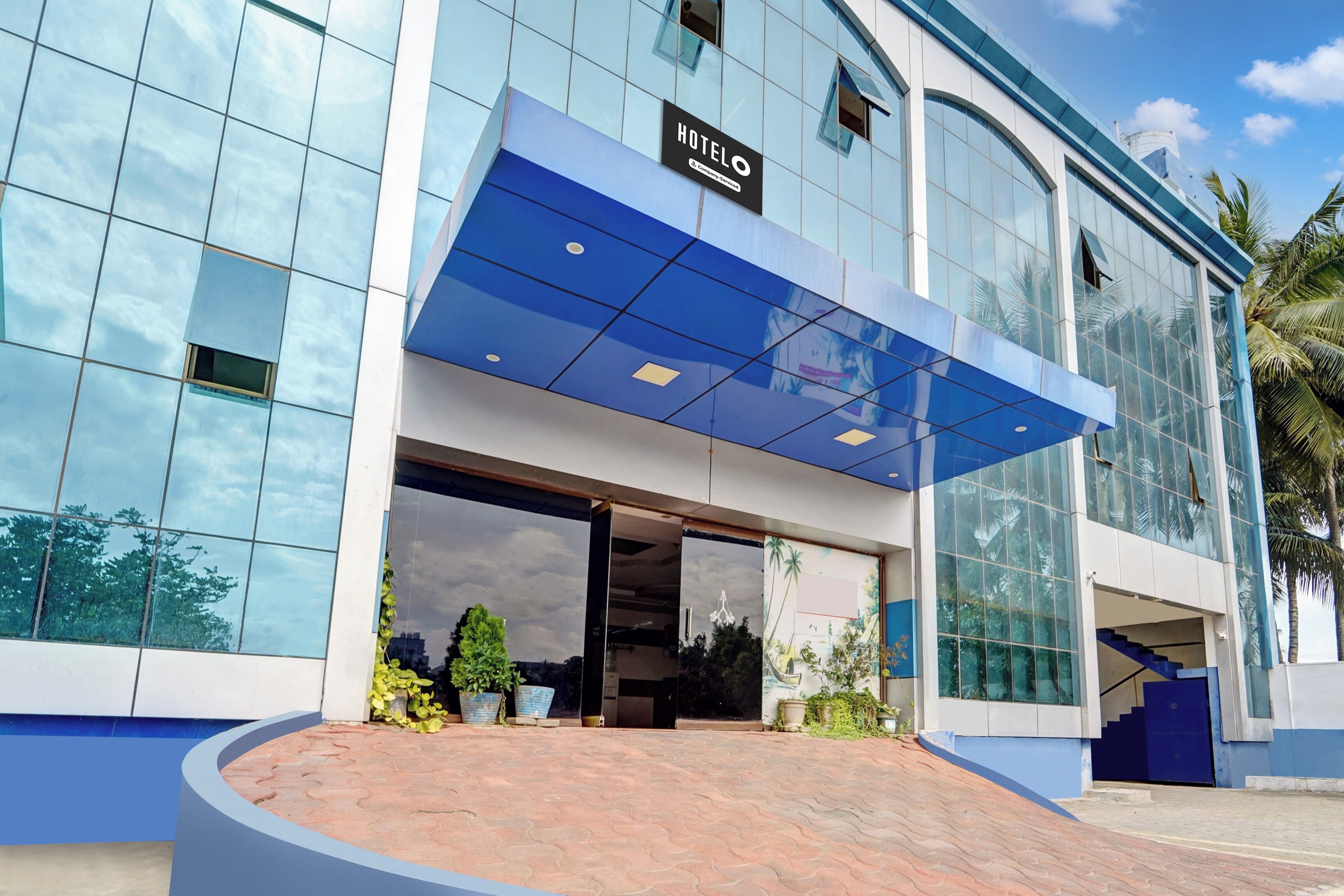 A modern hotel with a glass facade, a blue awning, and a sign indicating it's a company-serviced hotel.