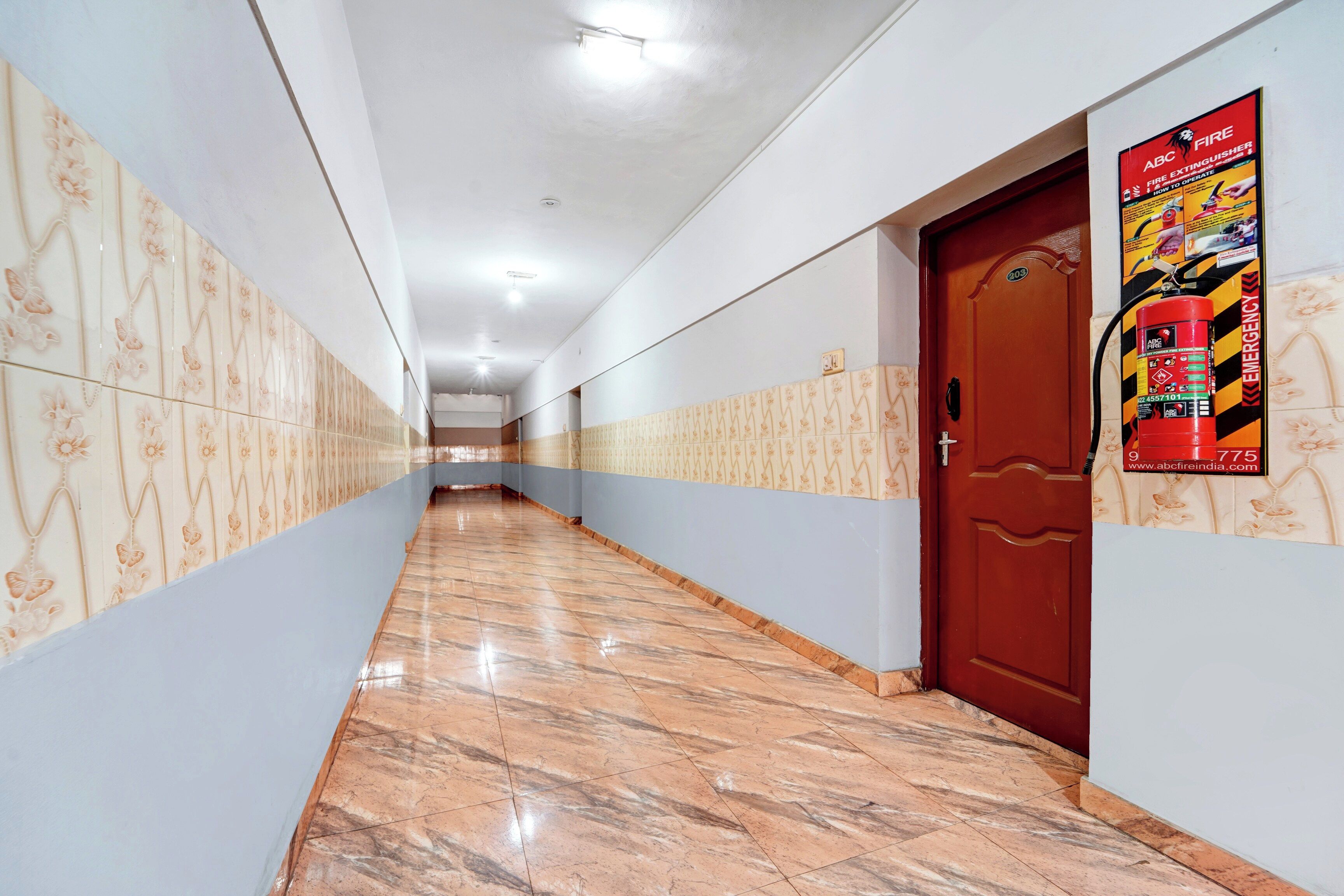 A corridor with patterned walls and a marble floor leading to a door with a fire extinguisher mounted on it.