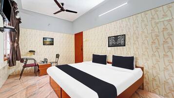 Quarto de hotel com cama, escrivaninha, cadeira, ventoinha no teto e janela com cortinas.