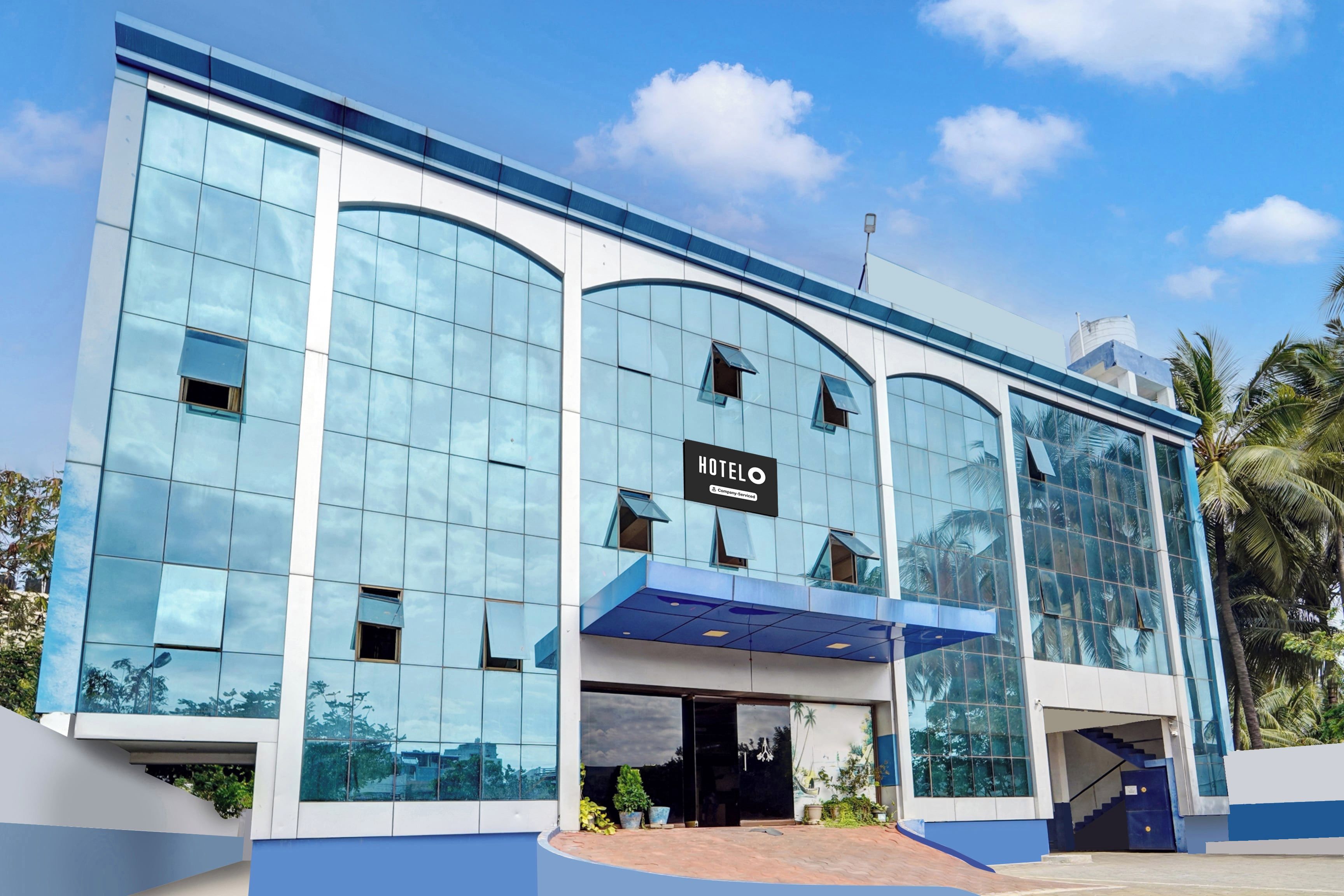 A modern hotel with a glass facade, a sign reading 'HOTEL', and a blue awning over the entrance.