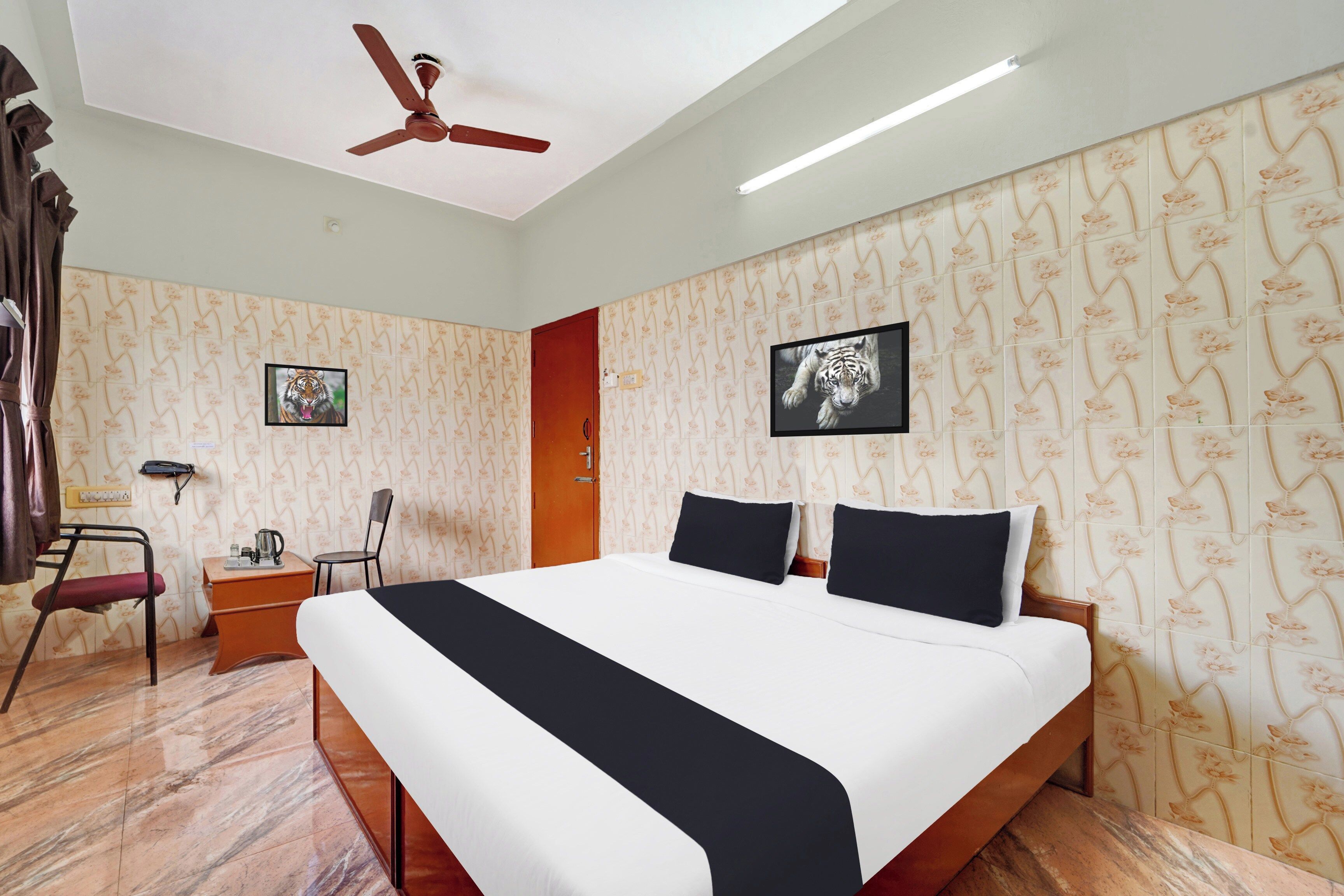 Habitación de hotel con cama, escritorio, silla, ventilador de techo y papel tapiz estampado.