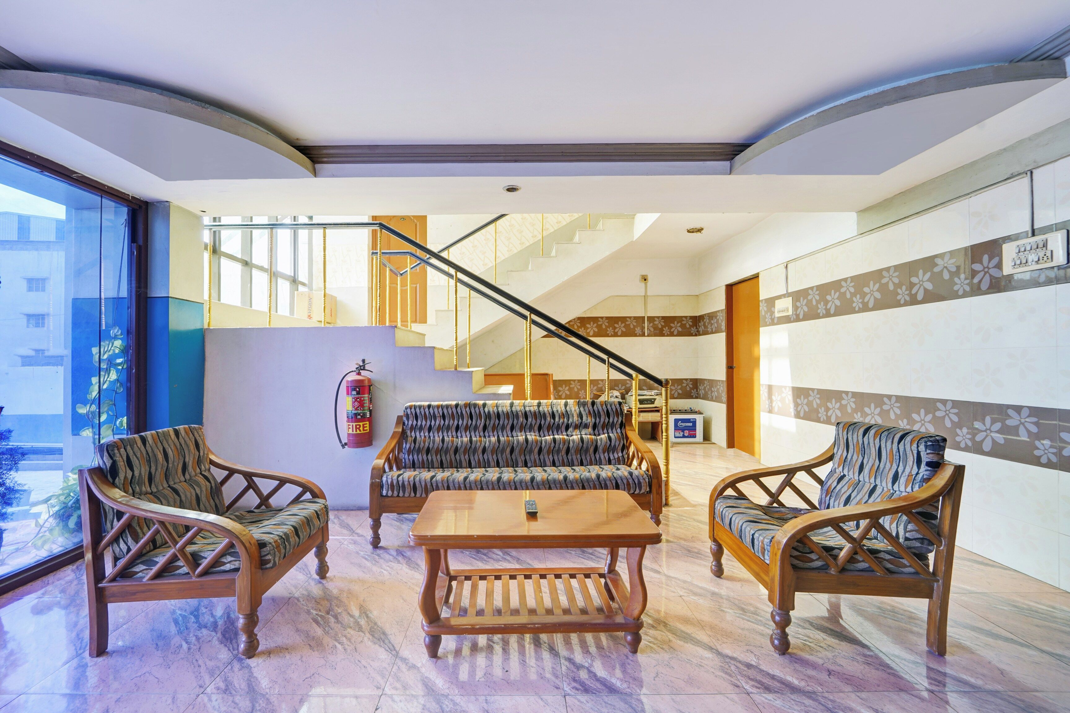 Et hotellobby med trappe, siddeområde og brandslukker.