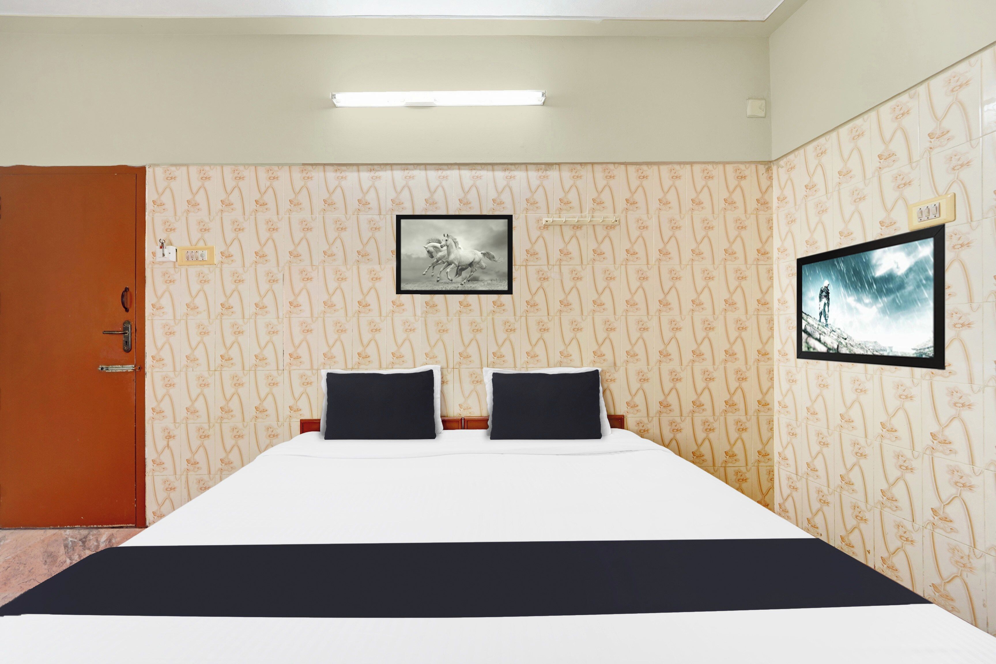 A hotel room with a bed, two black pillows, a framed picture on the wall, and a television.