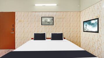 A hotel room with a bed, two black pillows, a framed picture on the wall, and a television.