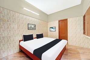 A bedroom with a bed, two pillows, a wooden door, and a wall-mounted TV. - Super Hotel O Tiruppur Near Railway (Tiruppur)